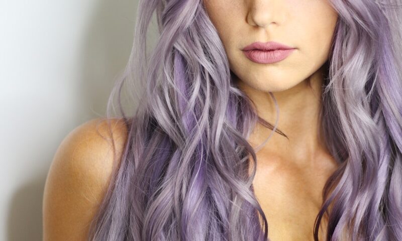 purple haired woman in black top leaning on wall